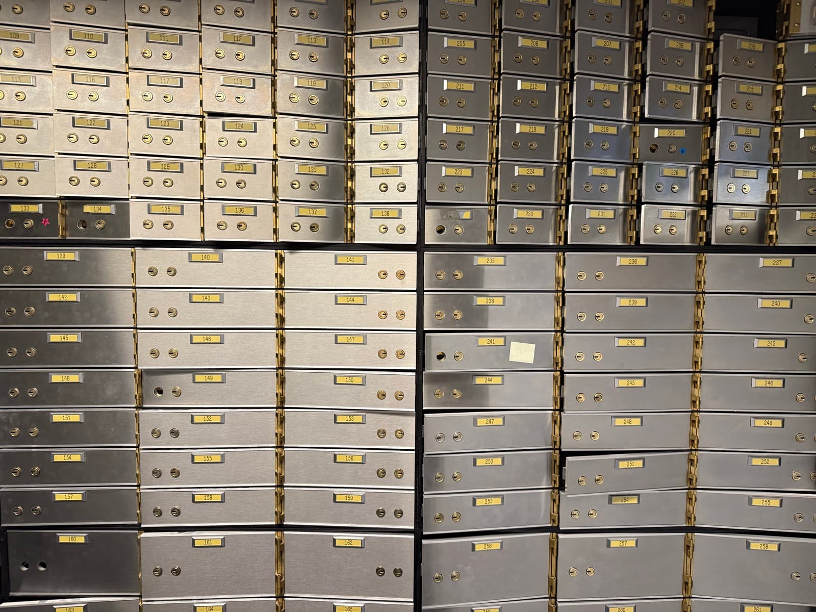 A wall of steel safe-deposit boxes with brass keyholes and numbered brass plates
